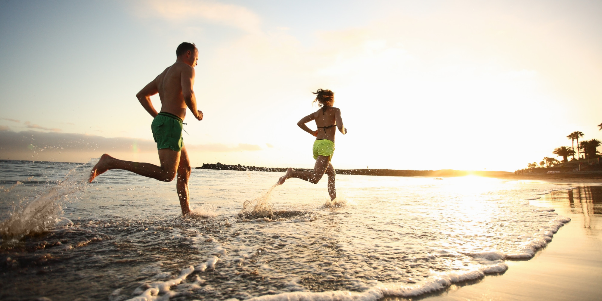 Man and woman running on beach at sunset